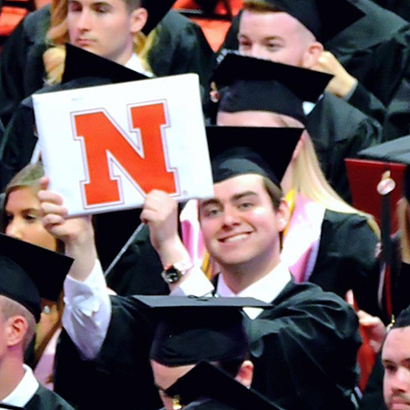 Lawrence Seminario holds up his diploma at UNL graduation.